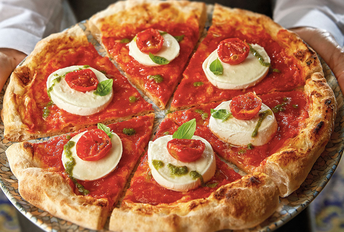 A waiter is holding a plate with a pizza cut into wedges.