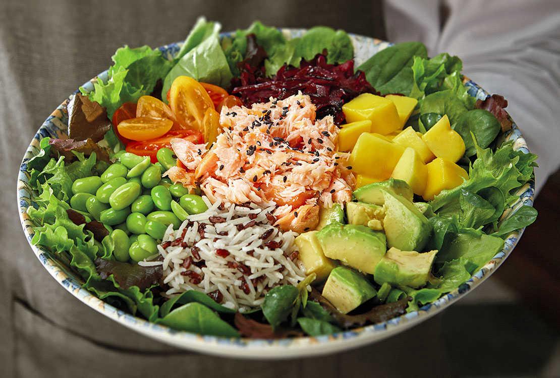 A waiter holds a plate containing a mixed salad in his hand.