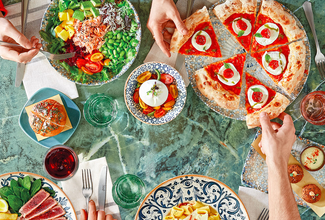 Persone sedute a tavola che mangiano vari tipi di piatti.