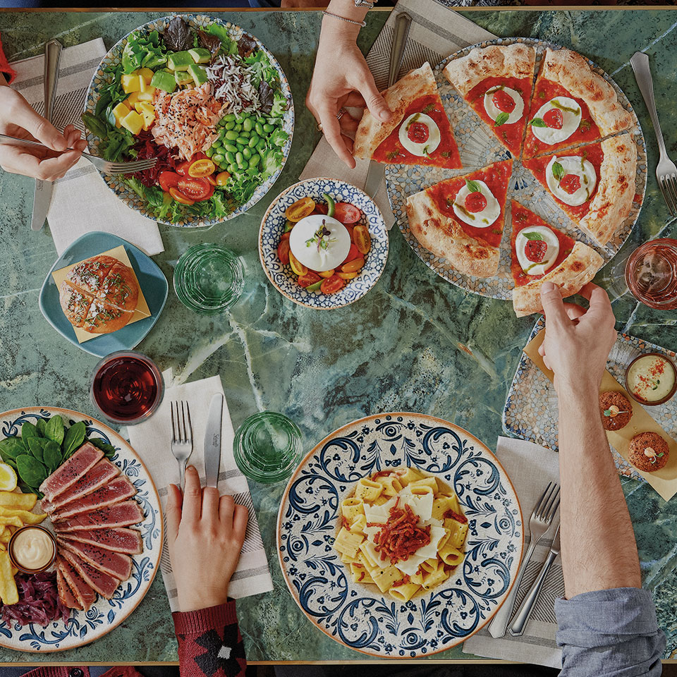 Persone sedute a tavola che mangiano vari tipi di piatti.