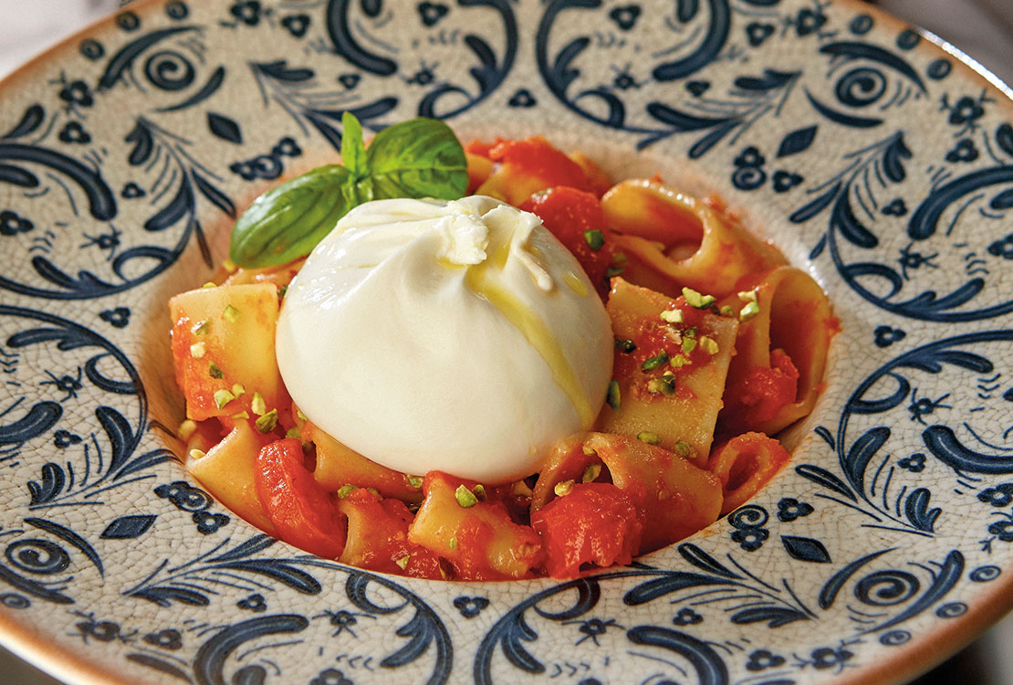 Piatto di pasta con salsa di pomodoro e burrata servito in un piatto di ceramica colorato.