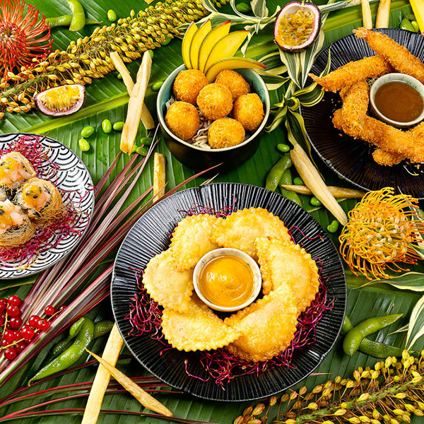 Composizione di vari piatti del menù appoggiati su foglie e con fiori intorno come decorazione.