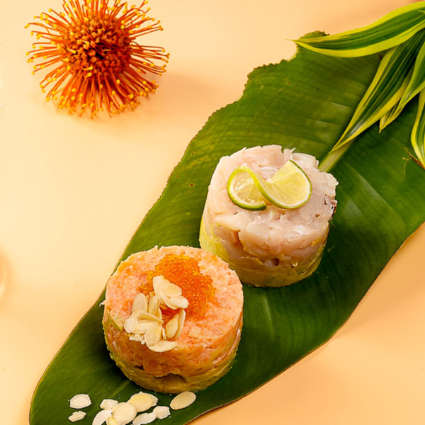 Due tartare di pesce appoggiate su una foglia. Attorno ci sono fiori e foglie.