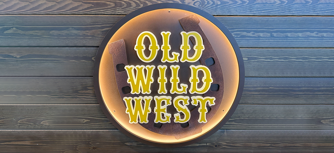 Insegna del locale Old Wild West, con scritta al led giallo su parete in legno